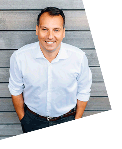 Dr. Giannakos, Gründer von OMOCURA, steht auf einer Treppe vor moderner Holzfassade